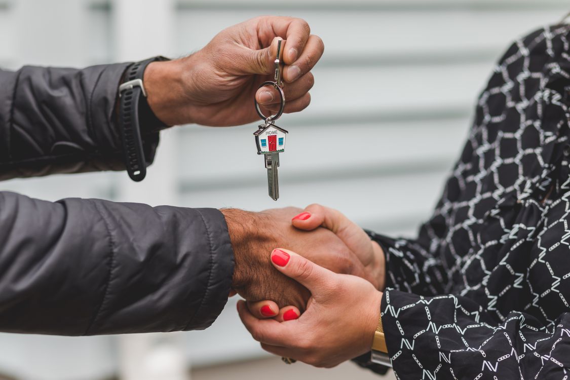 A close-up of a firm handshake between two people over a wooden desk, with a set of house keys visible, symbolizing a successful real estate agreement.