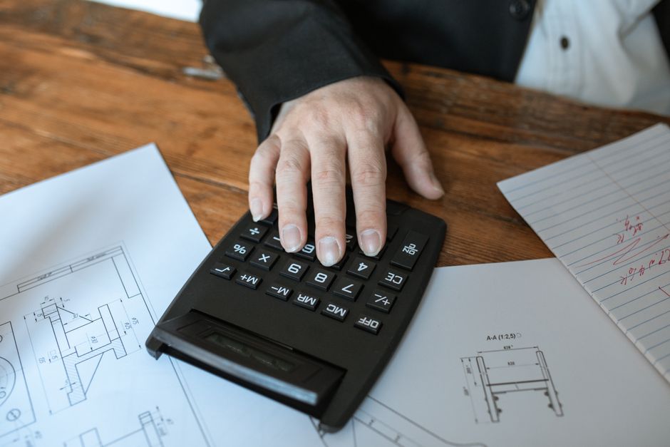 A close-up of hands using a calculator next to a set of house keys, symbolizing the financial hurdles of selling a home.