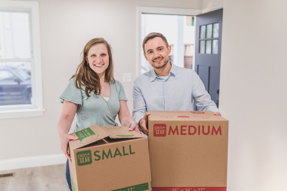A hopeful couple holding moving boxes and looking towards a bright future, illustrating the relief of overcoming financial barriers to sell their home.